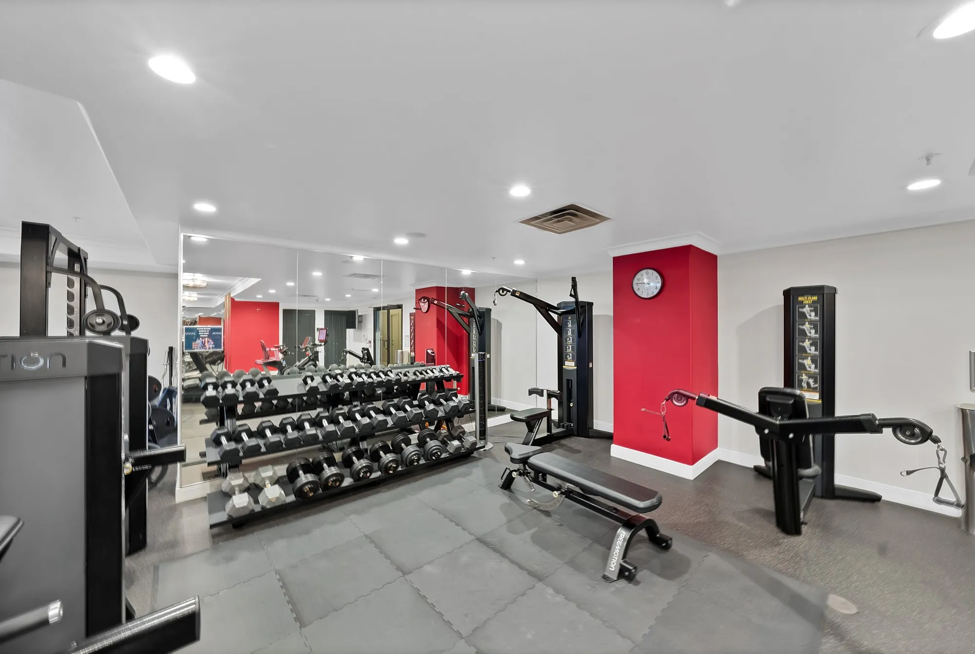Fitness center with mirrored wall, recessed lighting, red accent walls, and cushioned flooring