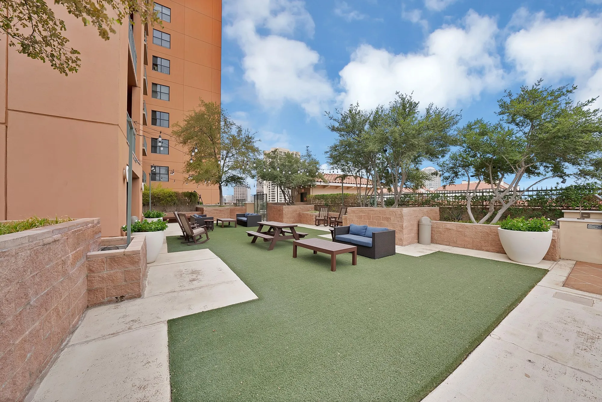 Expansive outdoor amenity deck featuring artificial turf, concrete paving, and built-in planters with mature trees
