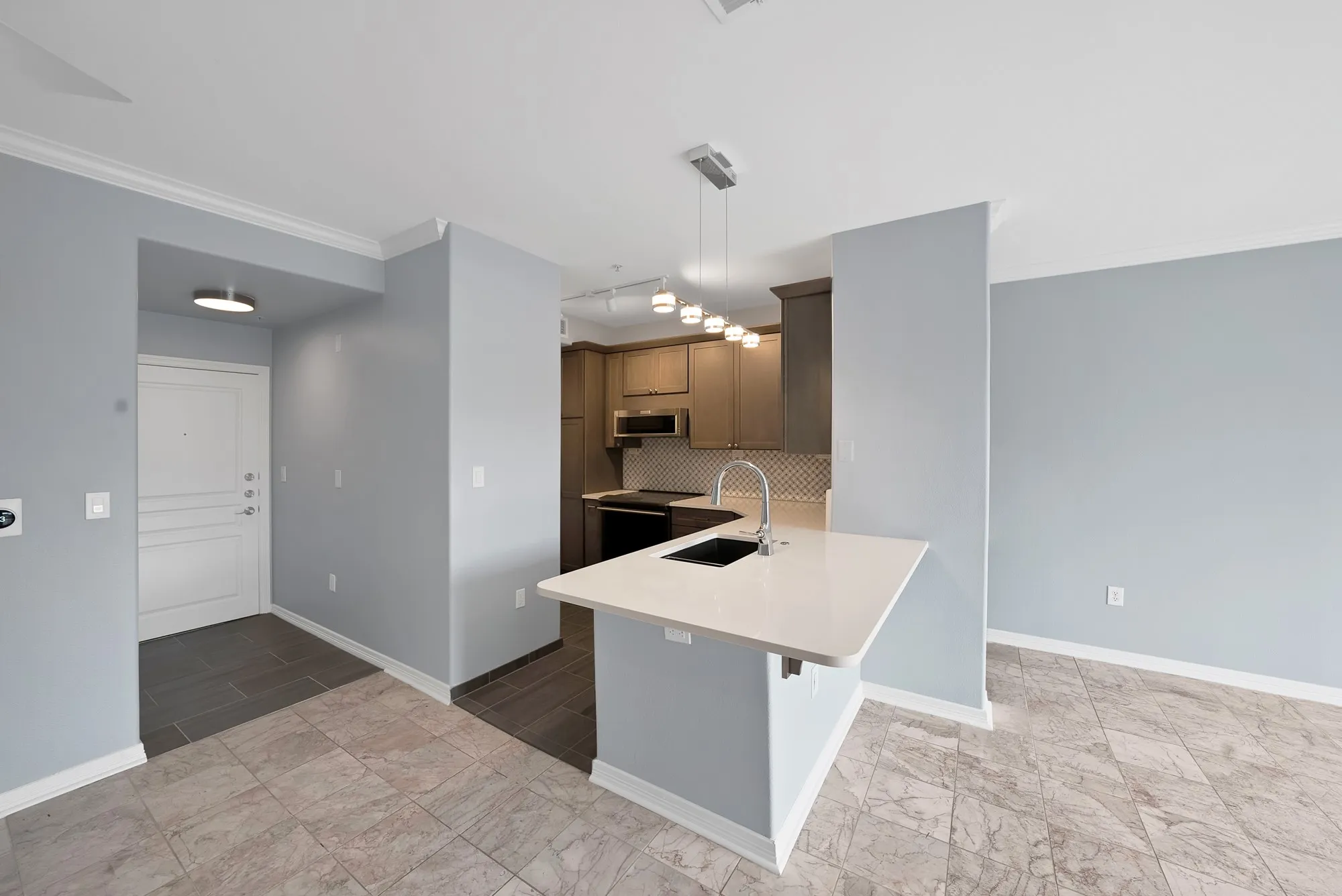 Kitchen island with a light-toned countertop, stainless steel sink, and modern pendant lighting