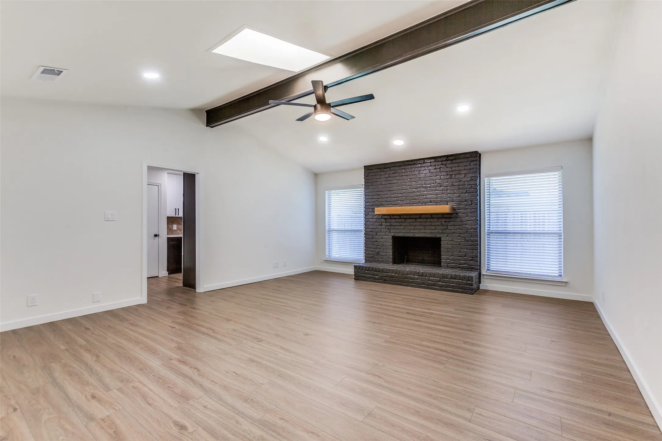 Unfurnished living room with ceiling fan, a fireplace, brick wall, light hardwood / wood-style floors, and lofted ceiling with skylight