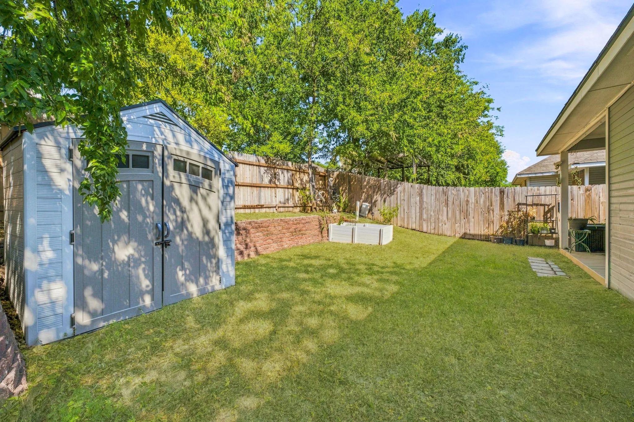Expansive backyard featuring a manicured lawn, wood privacy fencing, and a permanent storage shed