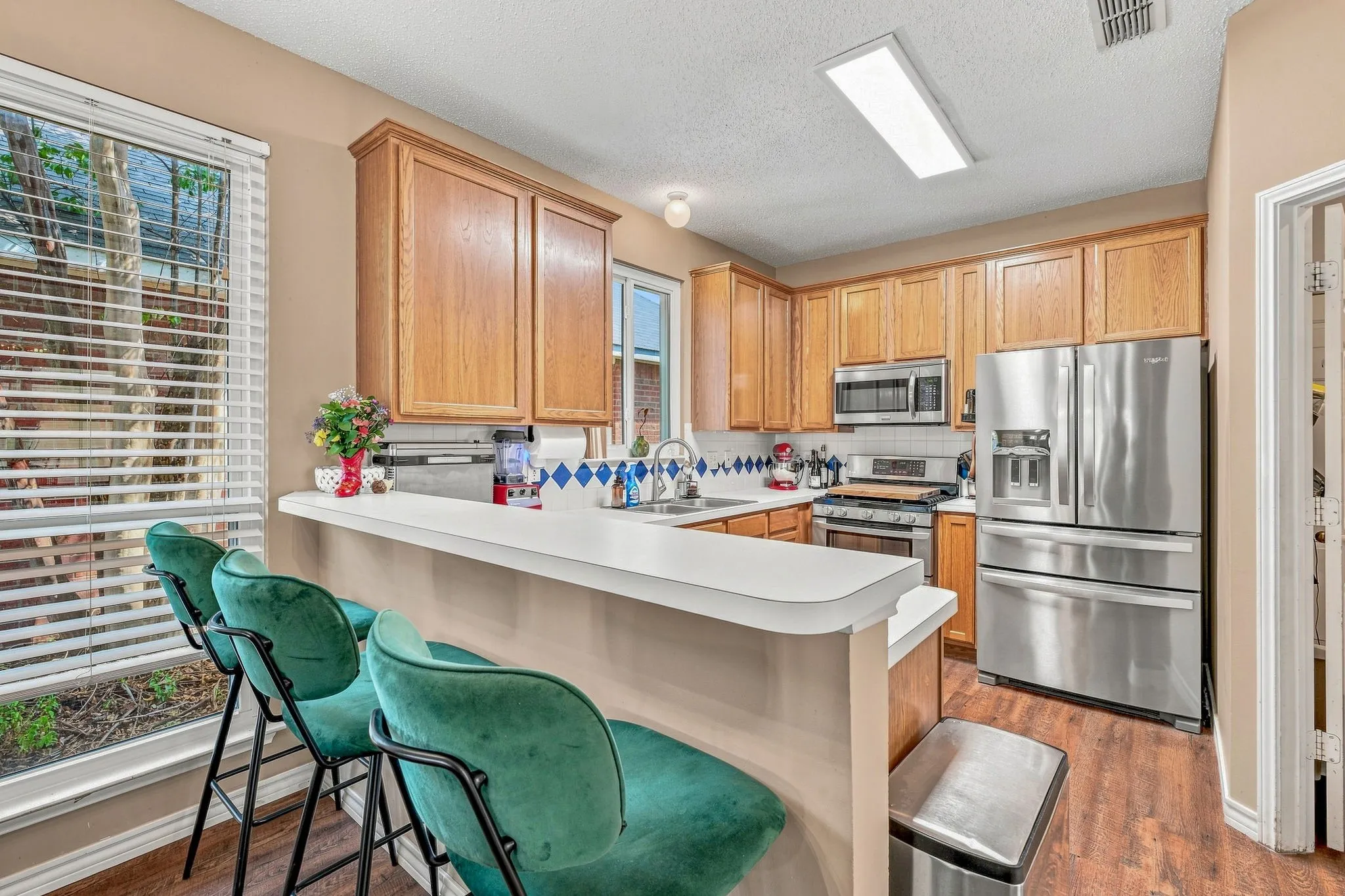 Kitchen featuring wood-finish flooring, a breakfast bar, wood cabinetry, stainless steel appliances, and a tile backsplash