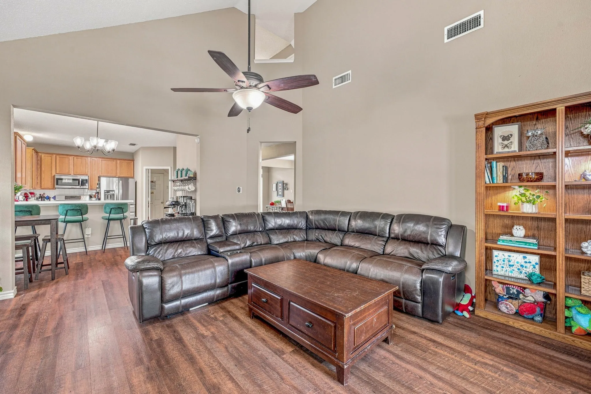 Vaulted ceiling, wood-finish flooring, built-in shelving, ceiling fan, and recessed kitchen with wood cabinetry
