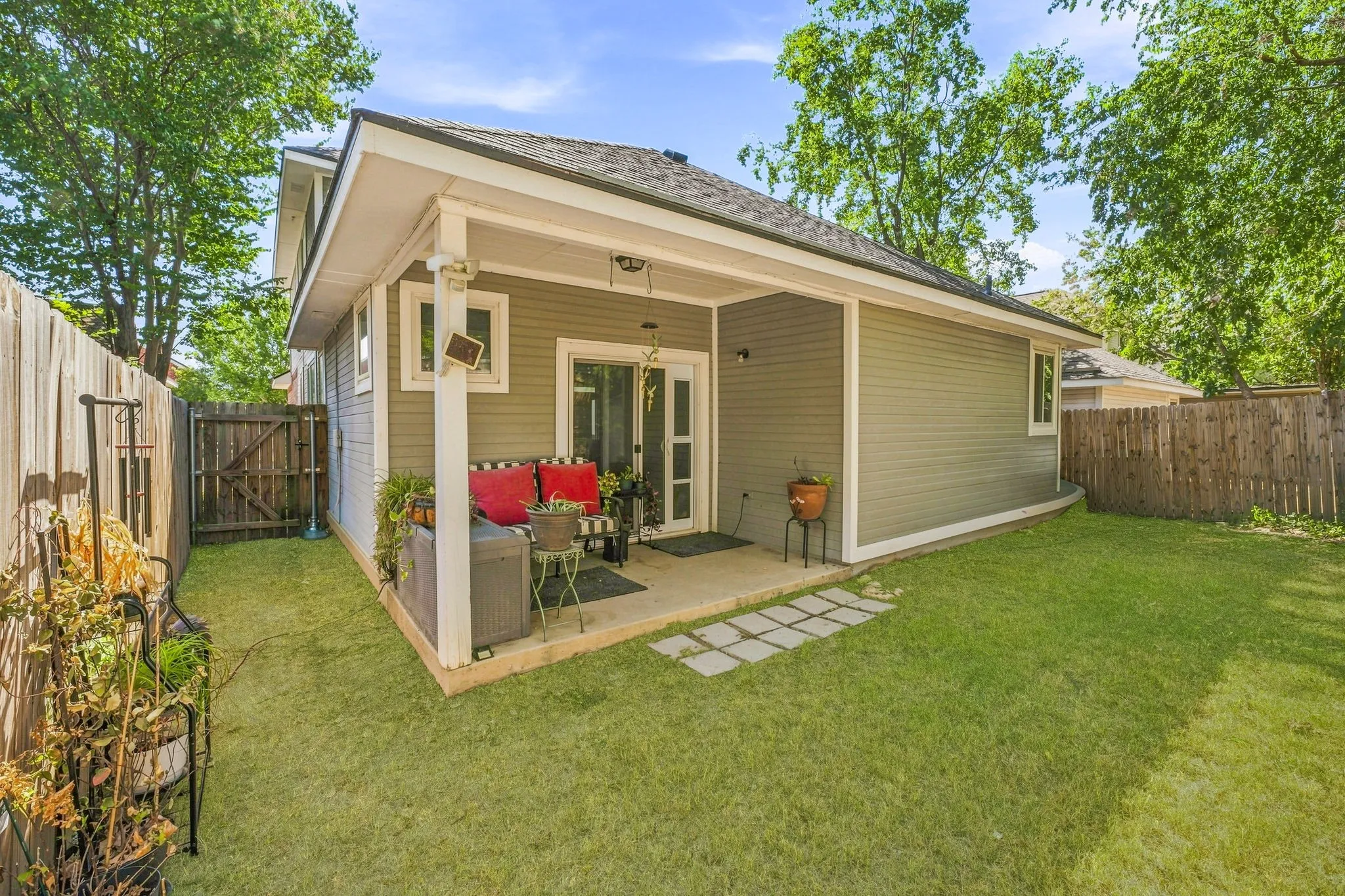Expansive backyard featuring a covered patio, sliding glass door, board and batten siding, privacy fencing, and stone paver accents