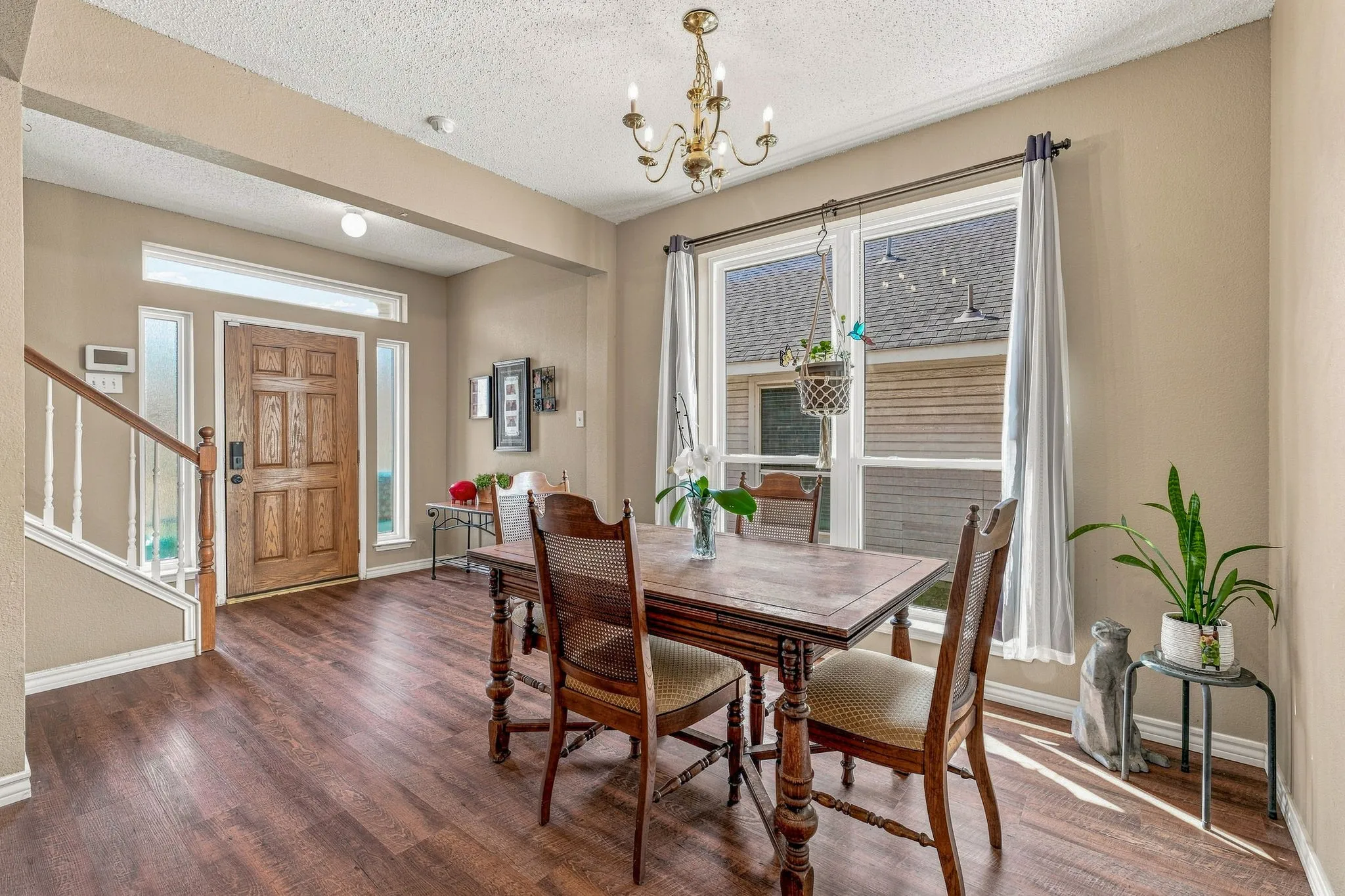 Wood-finish flooring throughout, solid wood front door with sidelights and transom window, traditional chandelier, and large window with vertical blinds