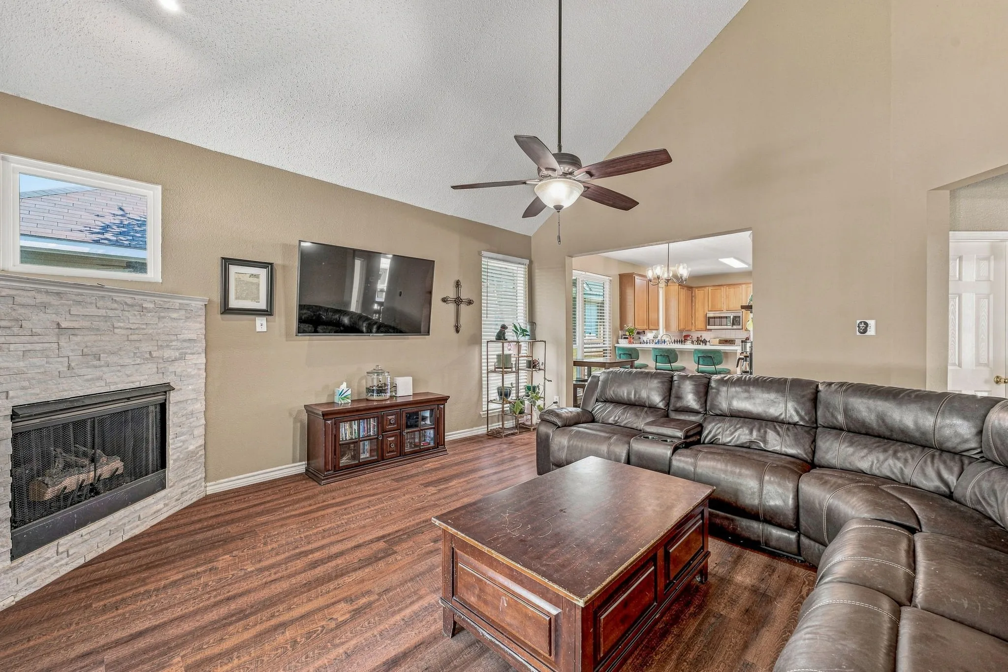 Vaulted ceiling, wood-finish flooring, stone-clad fireplace, ceiling fan, and open concept design