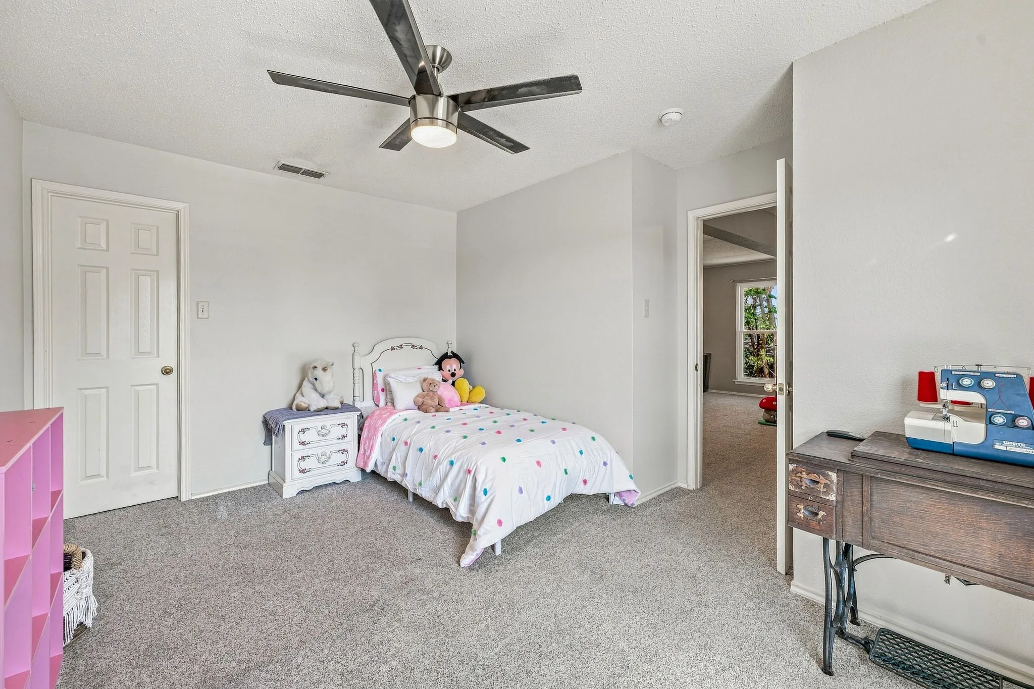 Neutral gray carpeting and walls, white paneled door, and a ceiling fan with integrated lighting