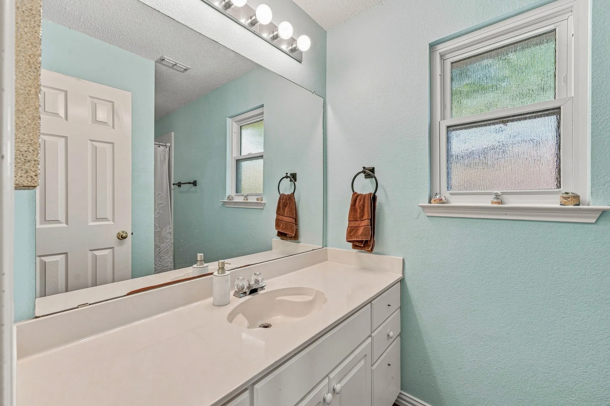 White vanity with integrated sink, full-width mirror, and a multi-bulb light fixture