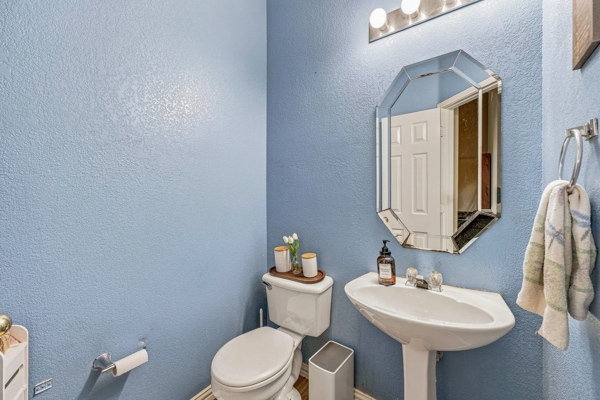 Pedestal sink with chrome-finish faucet, octagonal mirror, vanity bar lighting, and a white toilet
