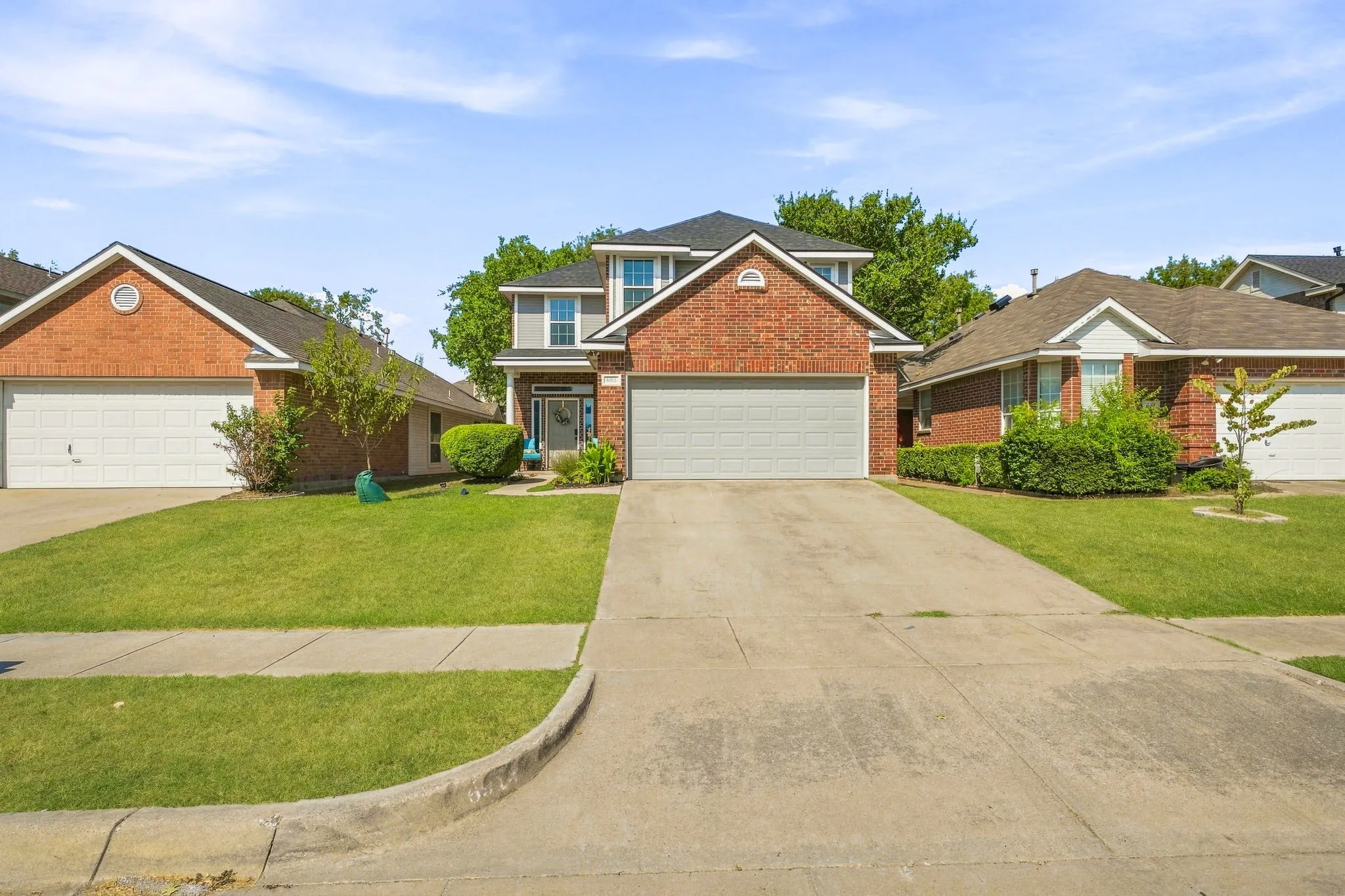 Brick and siding exterior with a two-car garage, concrete driveway, and established landscaping