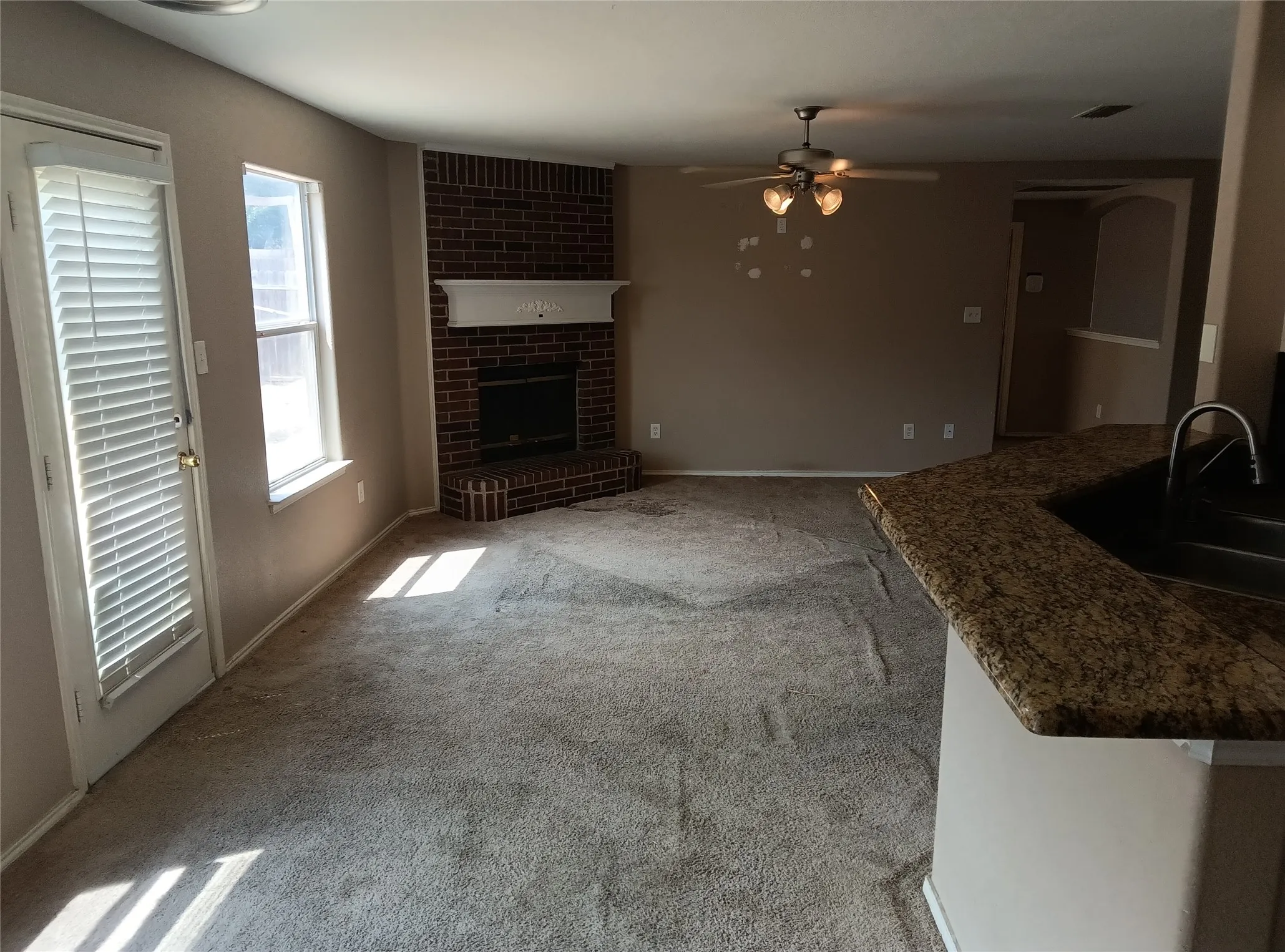 Brick fireplace with a white mantel, ceiling fan with integrated lighting, and a kitchen counter with an undermount sink and a high-arc faucet