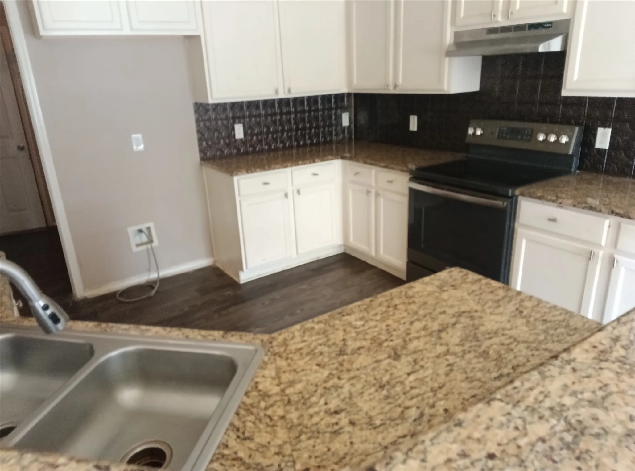 Kitchen featuring extensive countertops, white cabinetry, dark backsplash, a stainless steel double basin sink, and wood-finish flooring