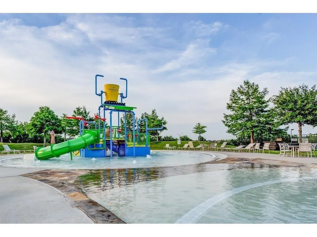 Splash pad with multiple water features and a green slide, surrounded by a concrete deck