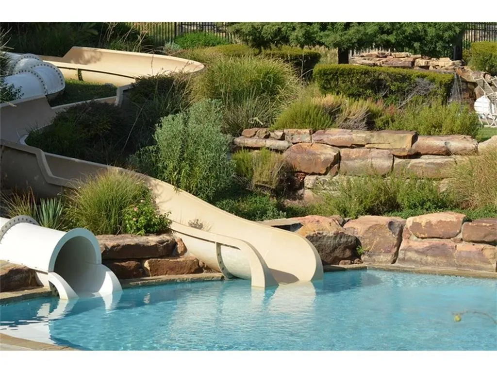 Swimming pool featuring two integrated water slides, natural stone retaining walls, and established landscaping