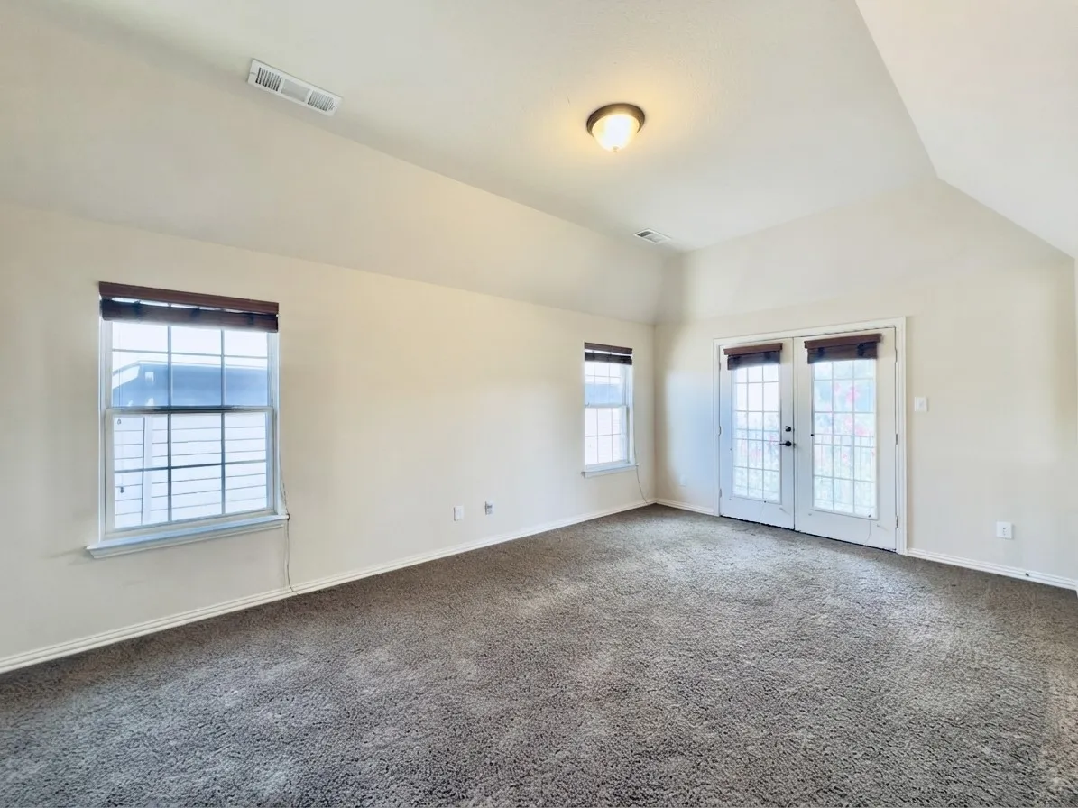 Vaulted ceiling, ceiling-mounted light fixture, carpet flooring, windows with blinds, and French doors