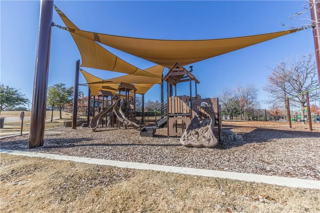 Playground area featuring shade structures, multi-level play equipment, slides, and wood chip surfacing