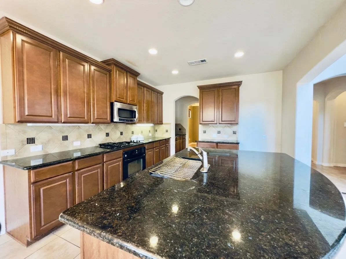 Kitchen with wood cabinetry, dark countertops, tiled backsplash, stainless steel microwave, and a gas range