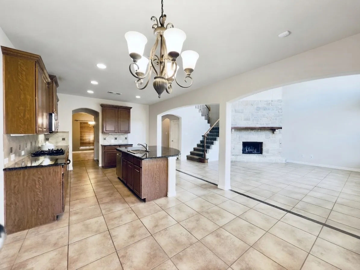 Kitchen featuring wood cabinetry, dark countertops, a central island with a sink, and tile flooring