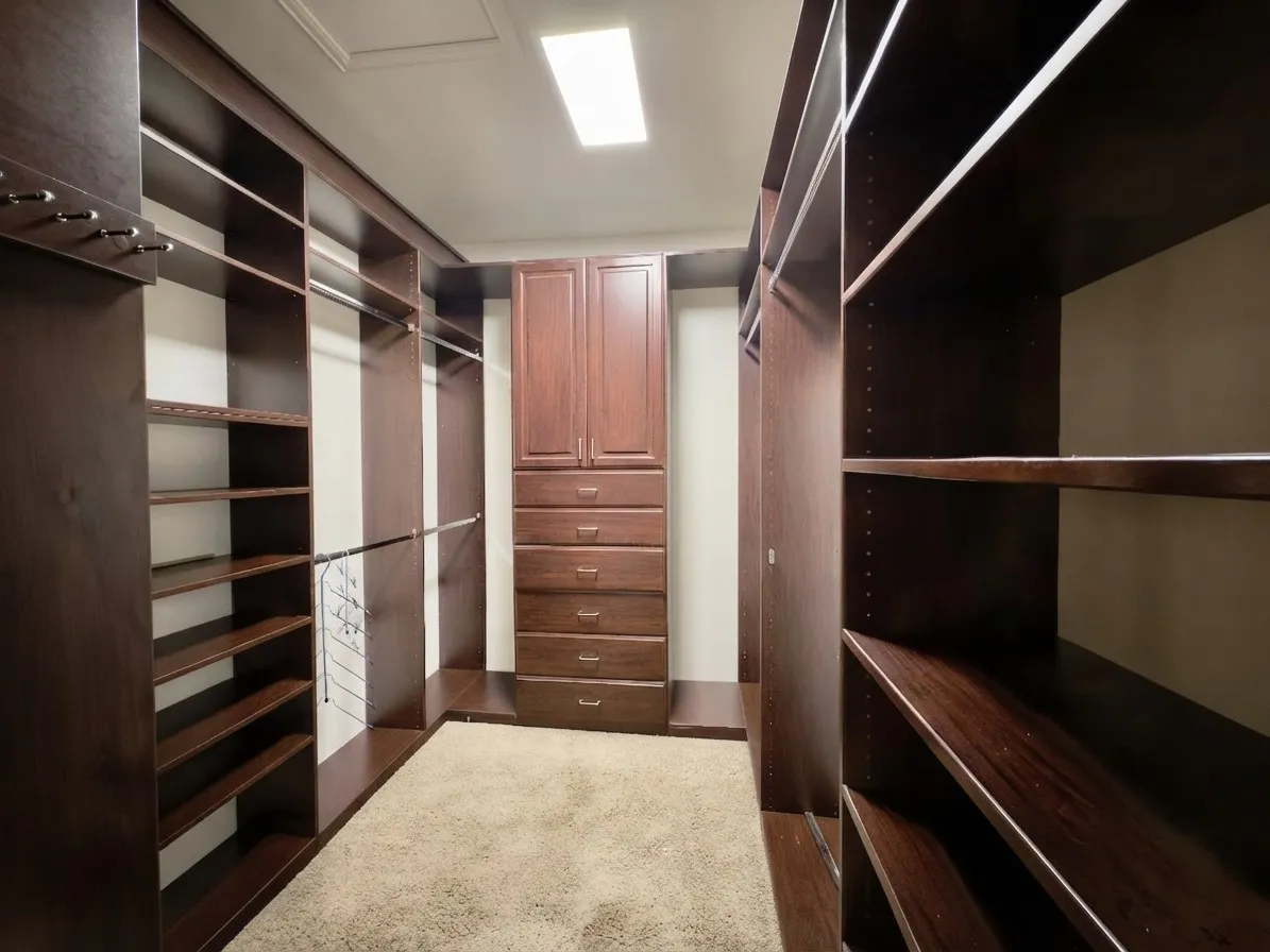 Custom dark wood-finish cabinetry, built-in shelving, chrome hanging rods, and integrated drawers