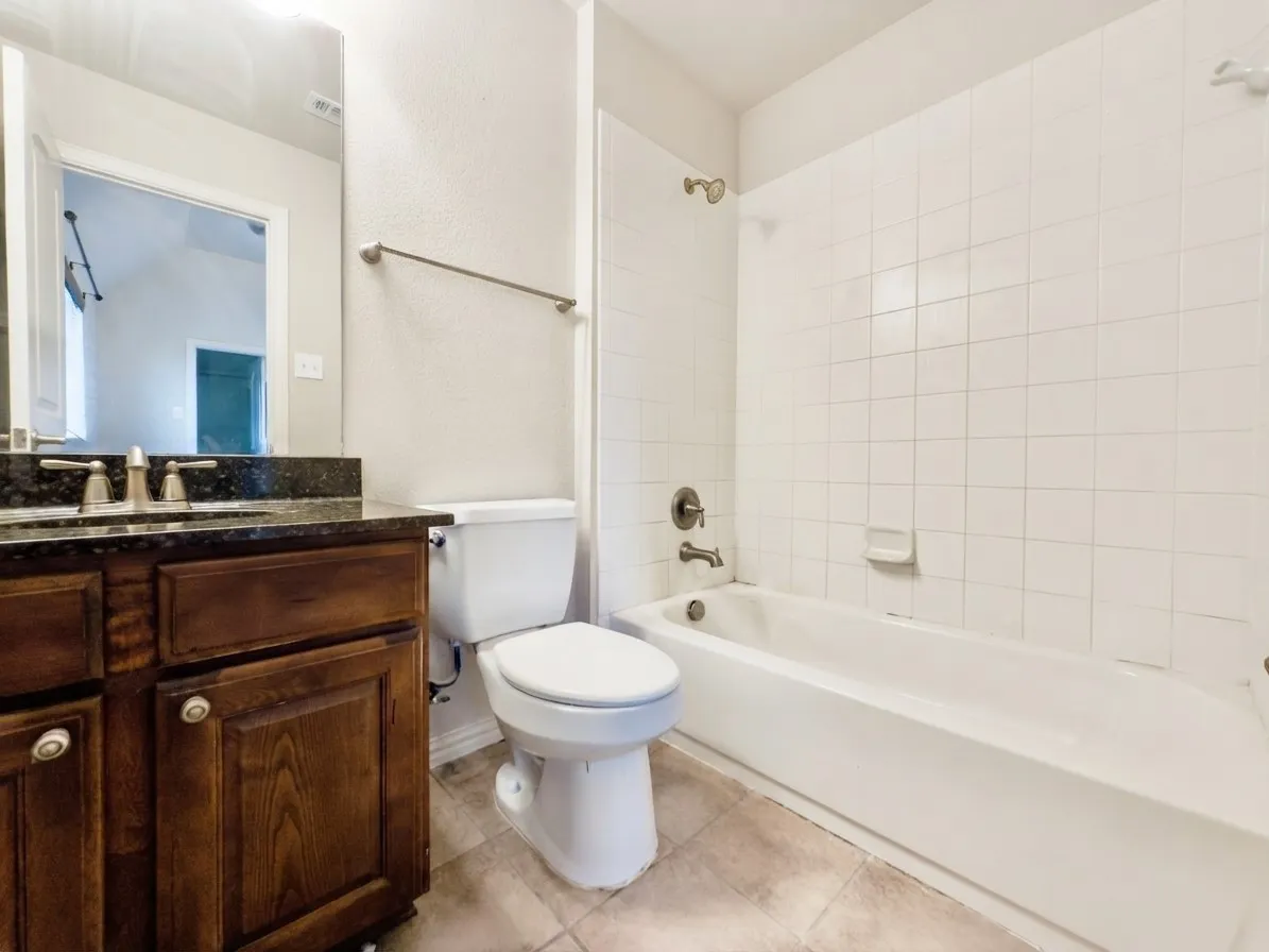 Wood-finish vanity with a dark countertop, undermount sink, and brushed nickel fixtures
