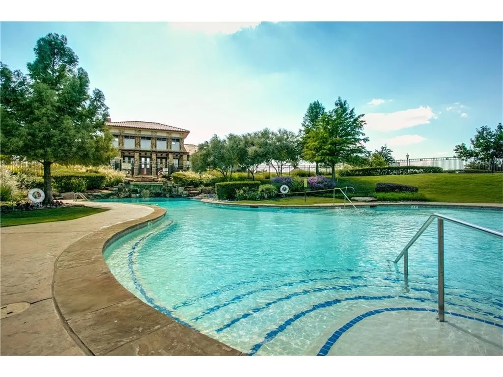 Curved swimming pool with mosaic tile accents, integrated waterfall feature, and surrounding landscaping
