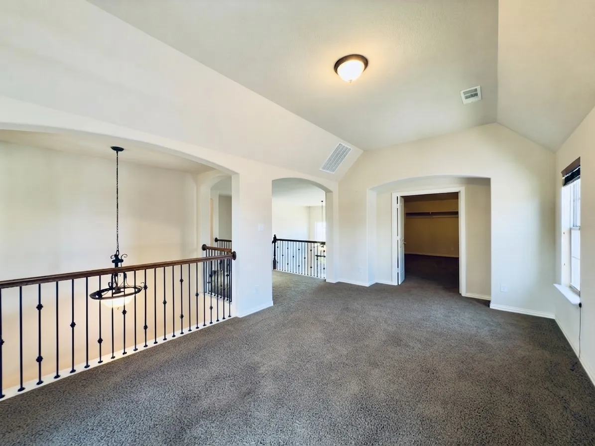 Carpeted upper-level landing with wrought iron and wood railing, arched doorways, a vaulted ceiling, and a prominent window