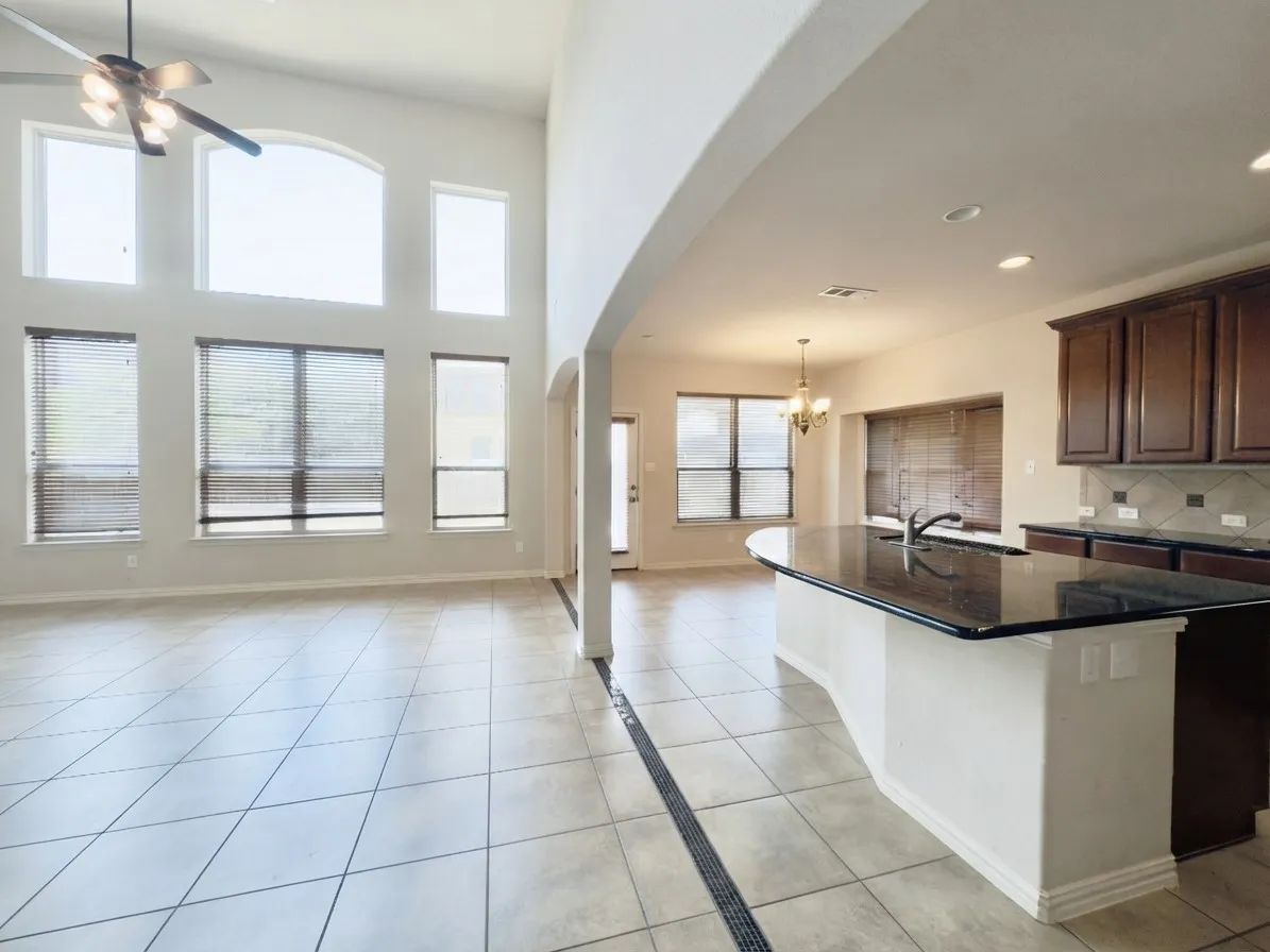 Vaulted ceiling with a ceiling fan, arched windows, tile flooring, kitchen island with sink and dark countertop, and dark wood cabinetry