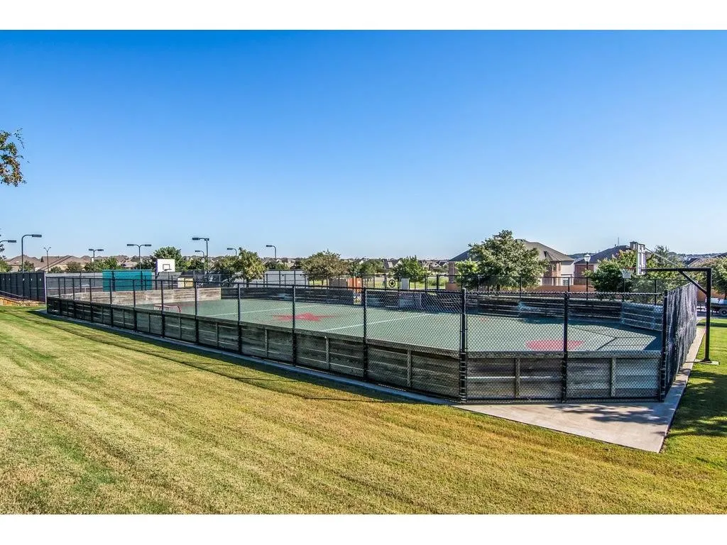 Recreational court featuring a perimeter fence, a basketball hoop, and overhead lighting fixtures
