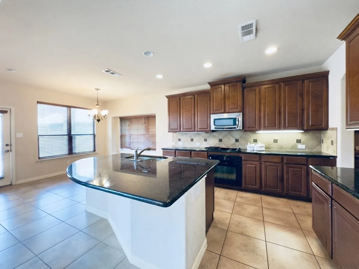 Kitchen featuring dark wood cabinetry, a granite island with an integrated sink, a tiled backsplash, and recessed lighting