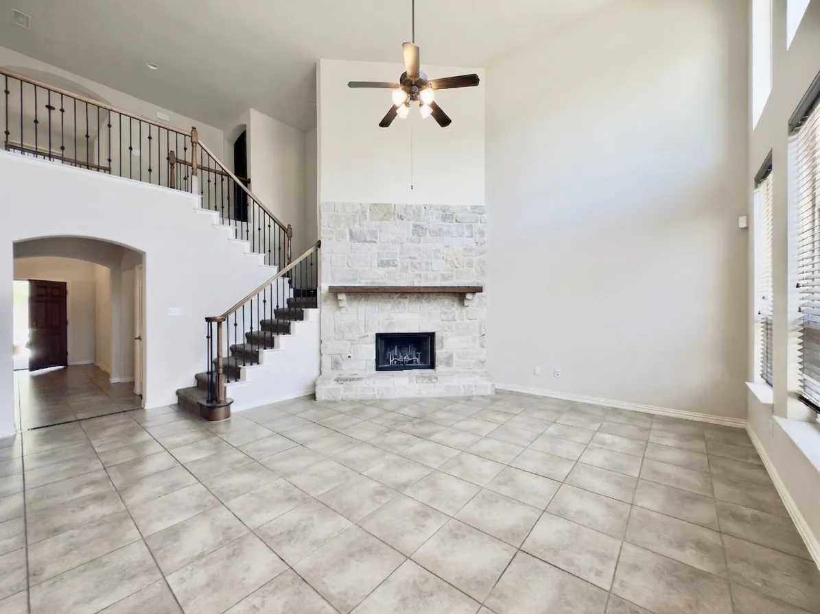 Two-story living area with stone fireplace, wood-finish mantel, and ceiling fan