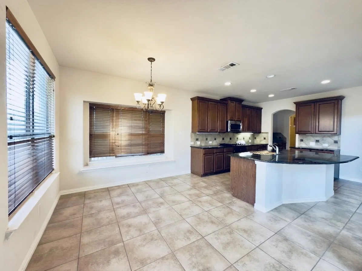 Kitchen and dining area featuring tile flooring, dark wood cabinetry, a kitchen island with a built-in sink, and a chandelier