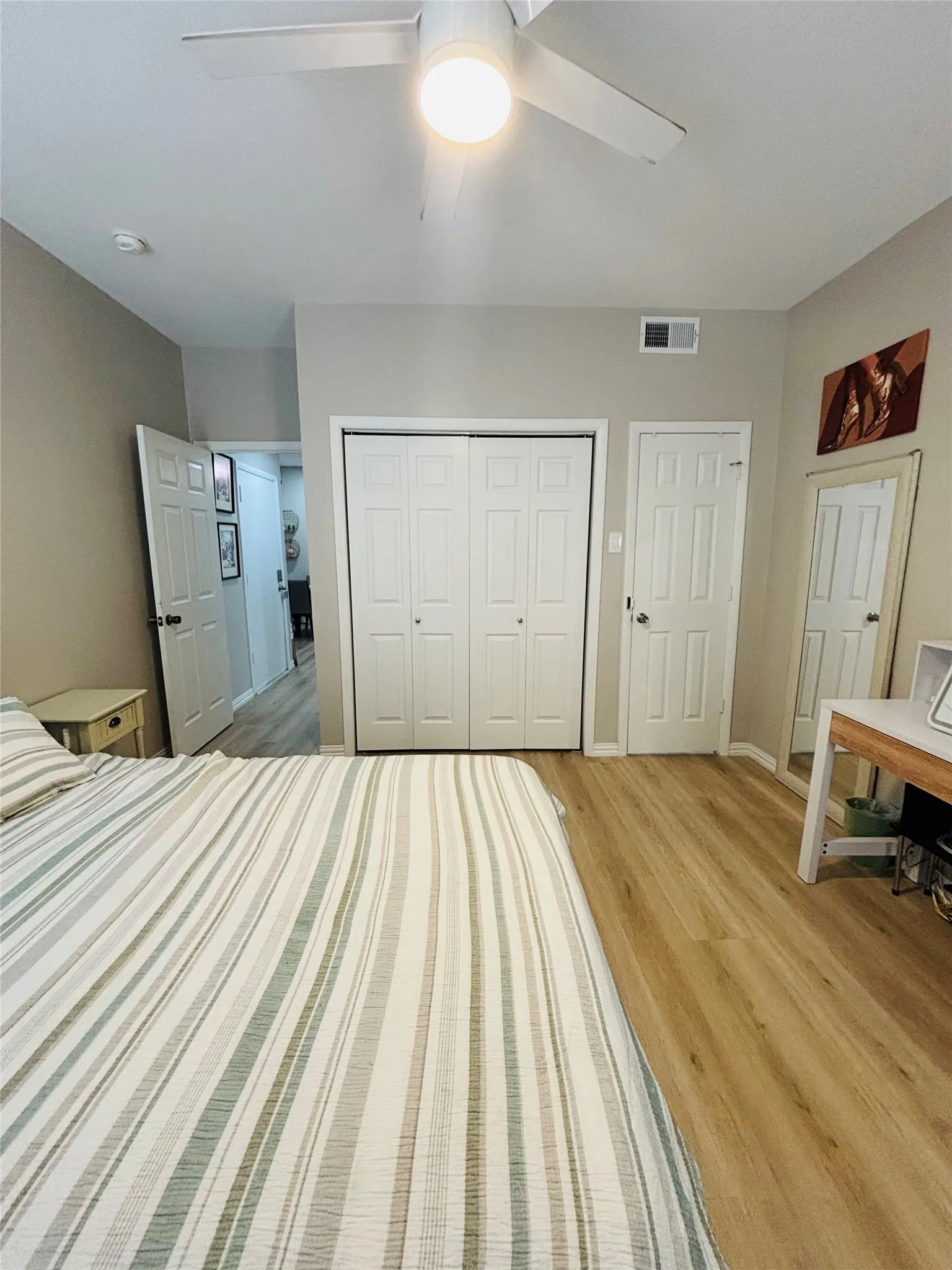 Wood-finish flooring with a ceiling fan light fixture and a built-in closet with bifold doors