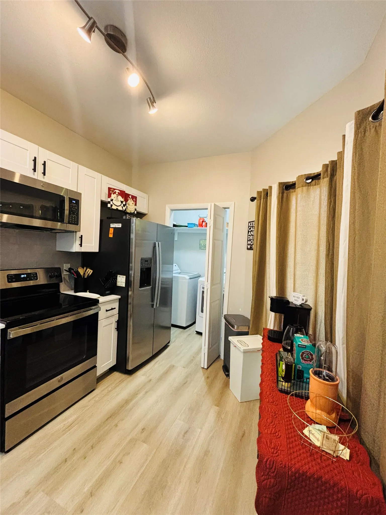 Kitchen featuring white cabinetry, stainless steel appliances, track lighting, and wood-finish flooring