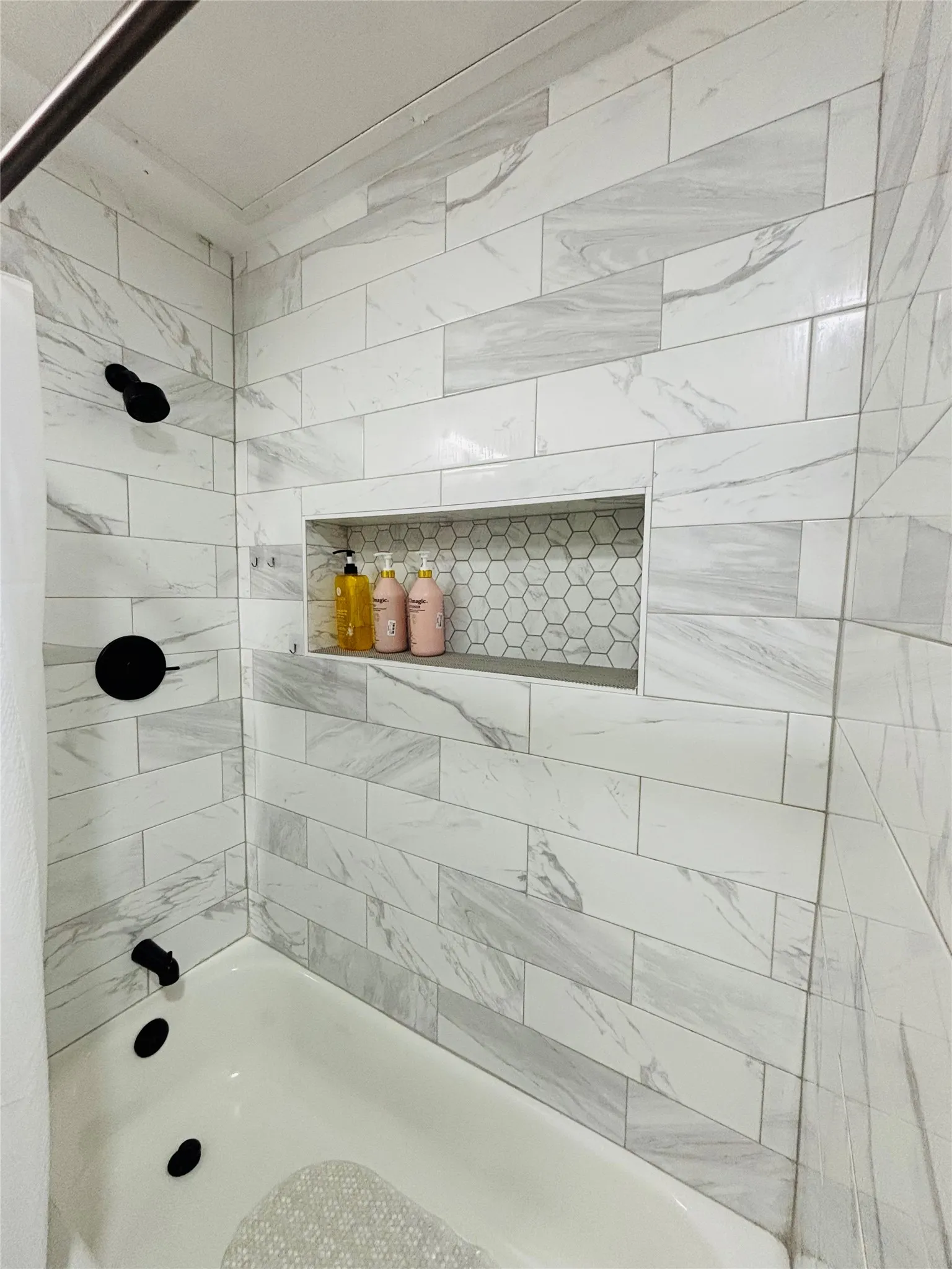 White subway tile with subtle gray veining, black matte fixtures, and a recessed shower niche with hexagonal tile