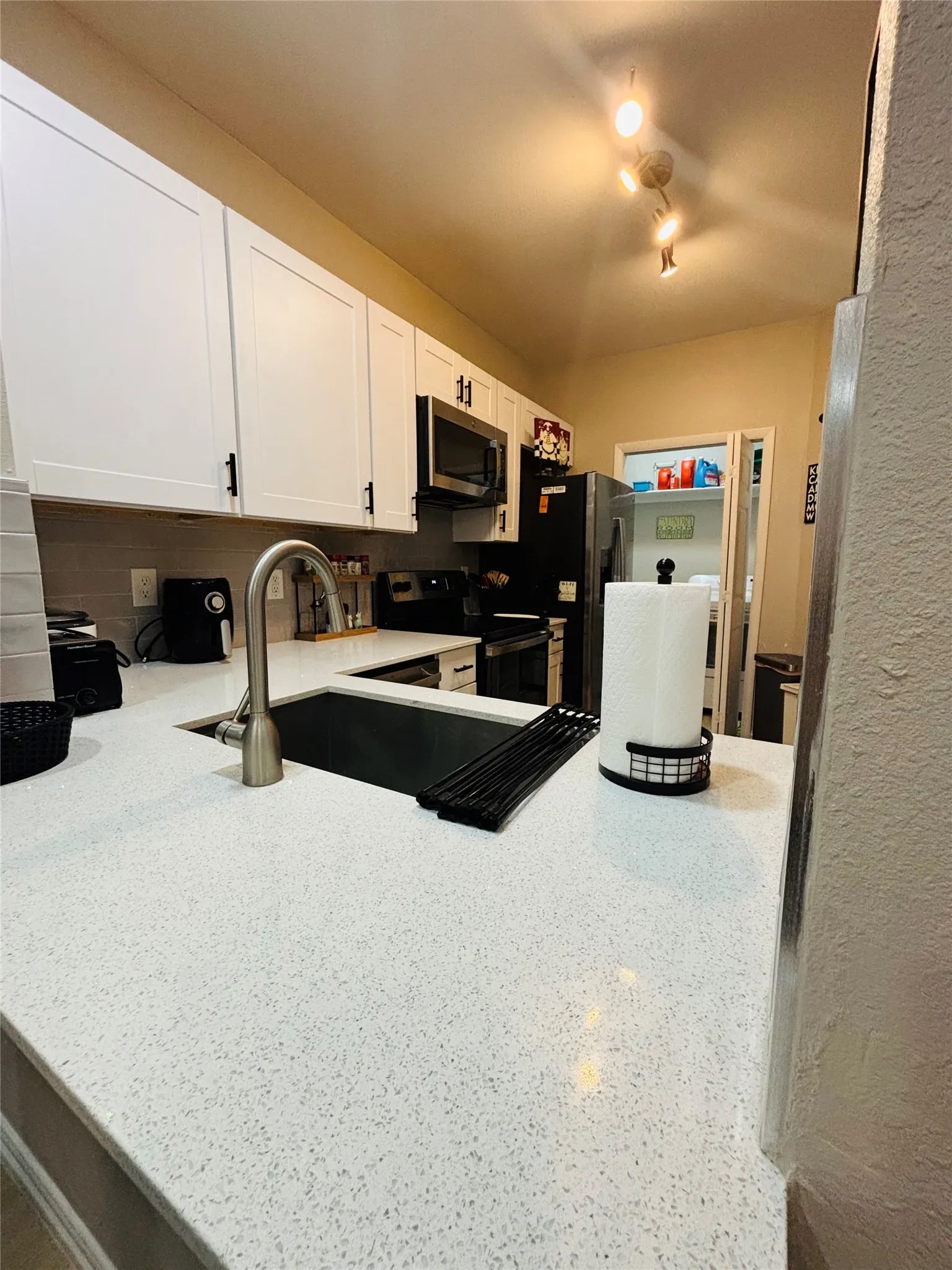 White shaker cabinetry, speckled countertops, stainless steel microwave, and an undermount sink with a gooseneck faucet