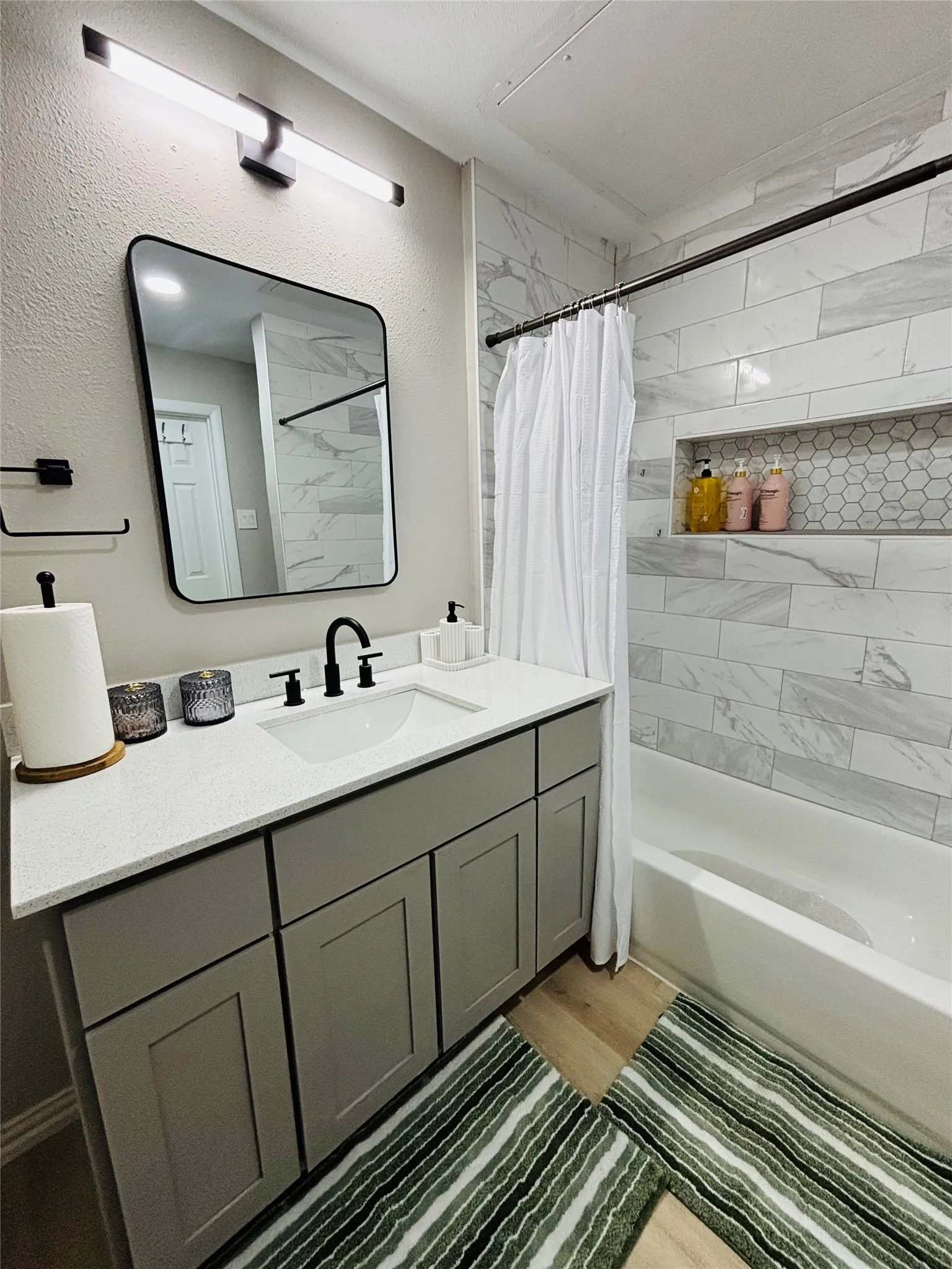 Bathroom with a single vanity featuring a white countertop and gray cabinetry, black fixtures, and wood-finish flooring