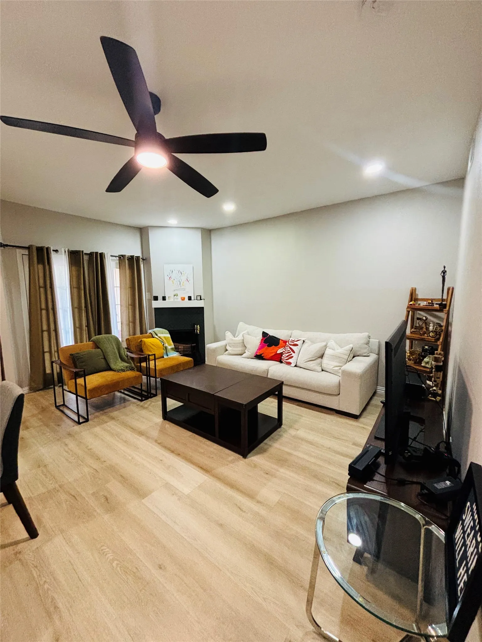 Wood-finish flooring, recessed lighting, ceiling fan with integrated light, and a built-in fireplace with a dark mantel