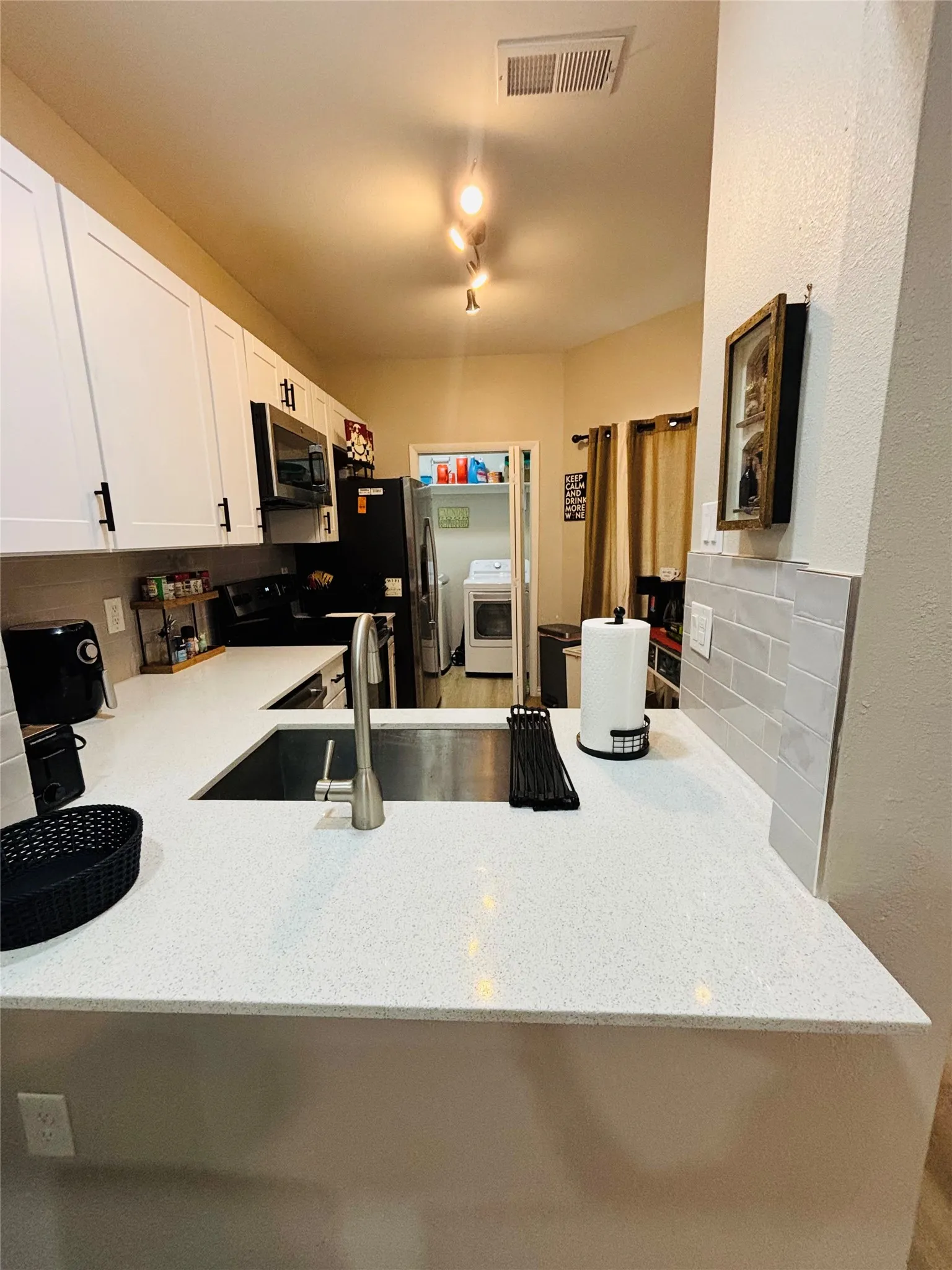 White upper and lower cabinetry, stainless steel undermount sink, gooseneck faucet, light-toned countertop, and light gray subway tile backsplash