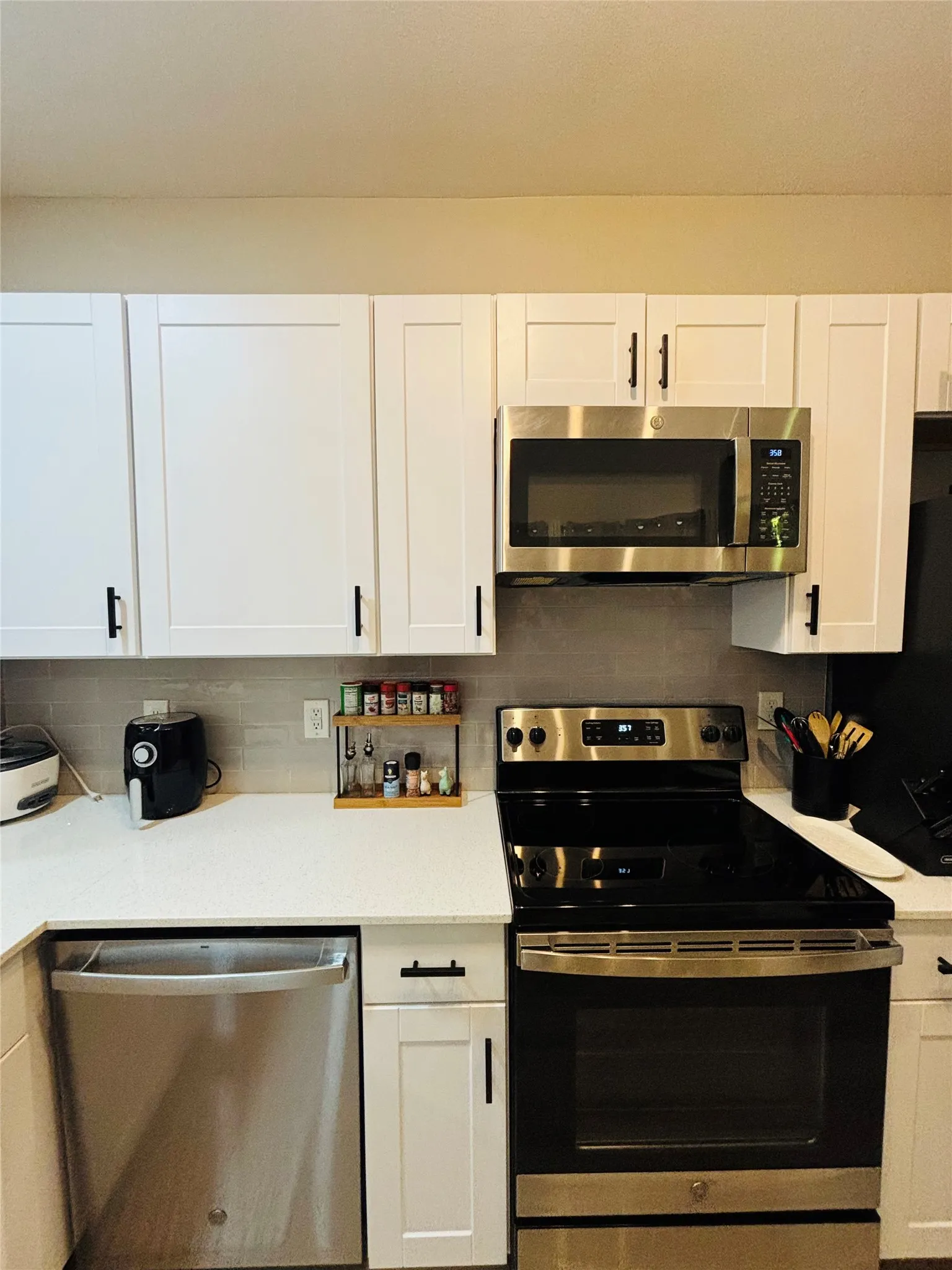 White shaker-style cabinetry, solid surface countertops, stainless steel appliances, and a tiled backsplash