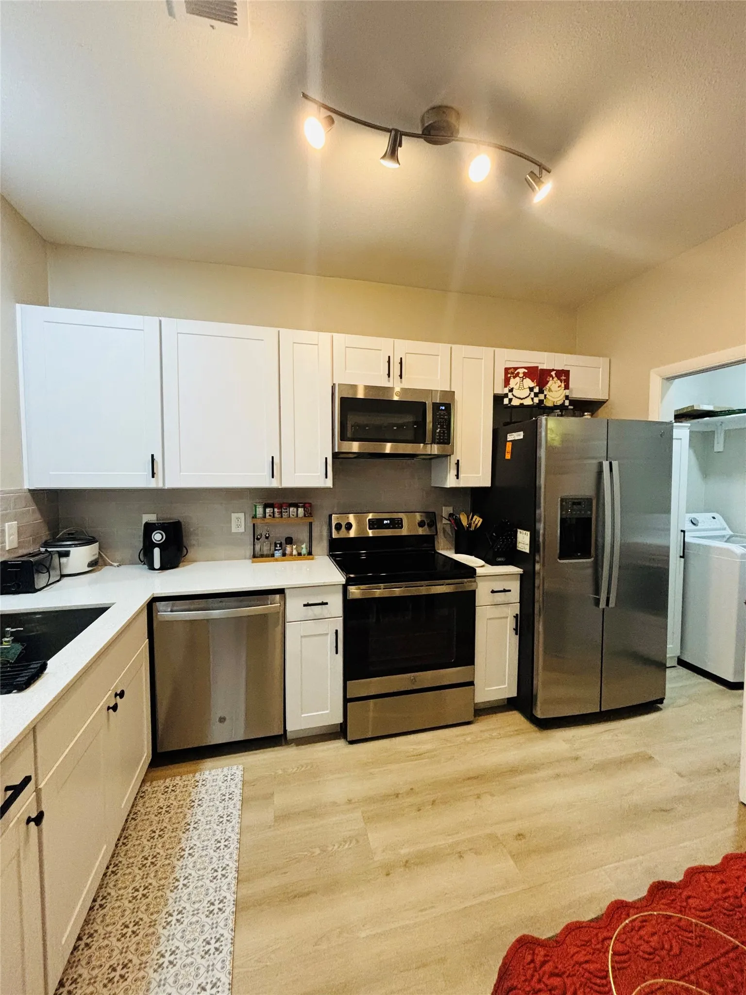 Kitchen featuring stainless steel appliances, white cabinetry, track lighting, light-toned wood-finish flooring, and a tiled backsplash
