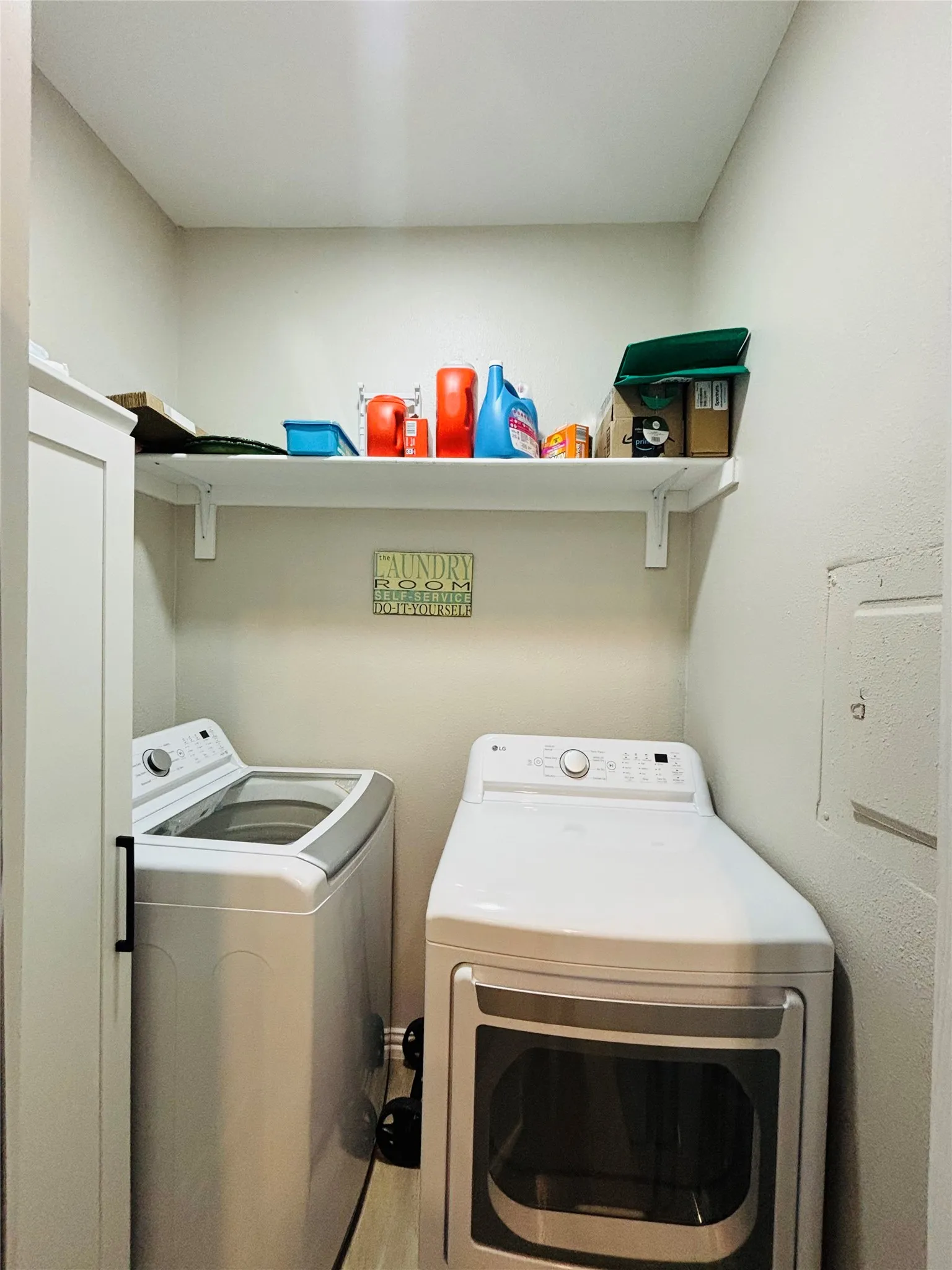 Dedicated laundry area with light-colored walls, overhead shelving, and wood-finish flooring