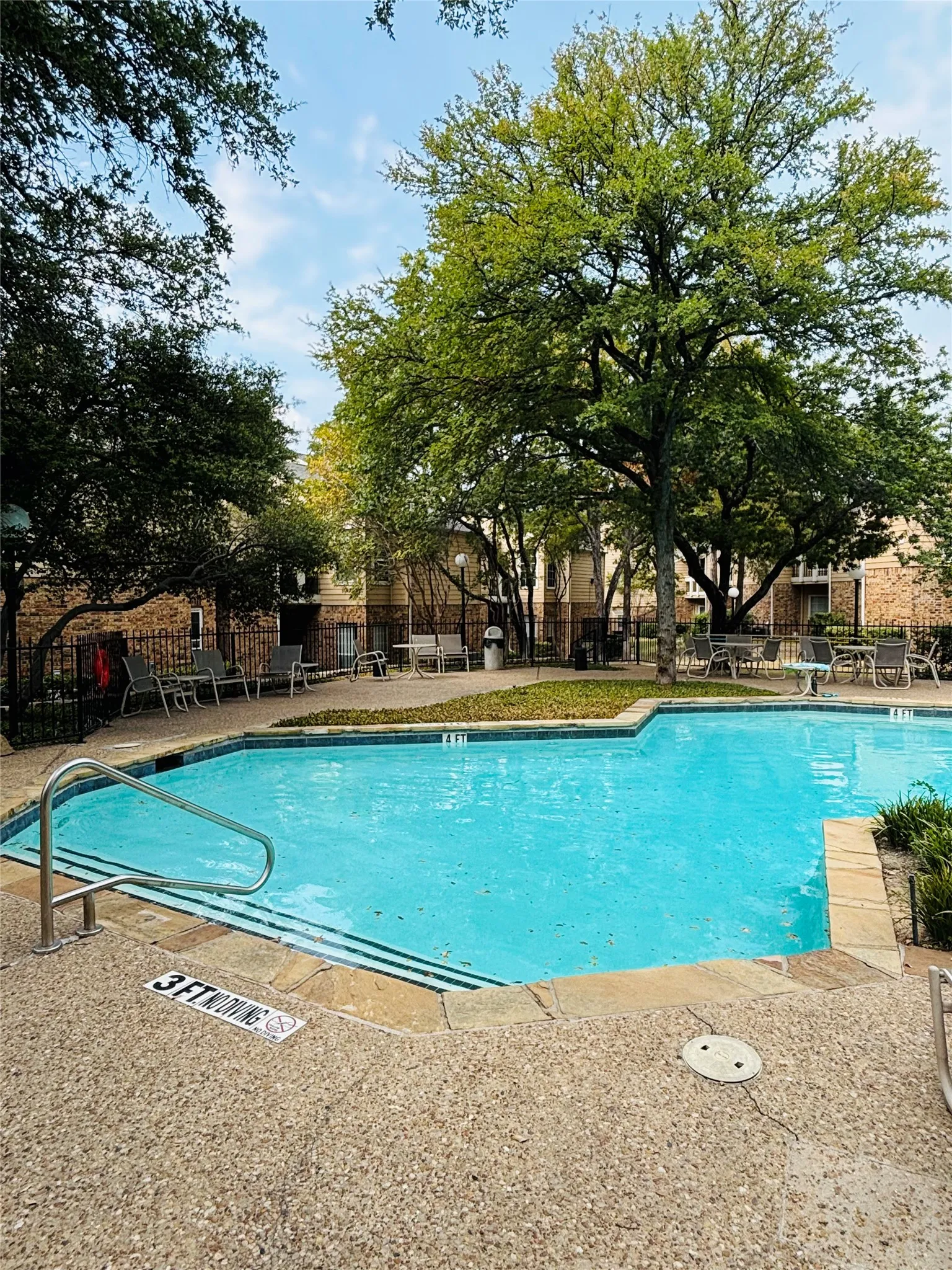 Inviting swimming pool with integrated steps and a stainless steel handrail, surrounded by a textured aggregate deck