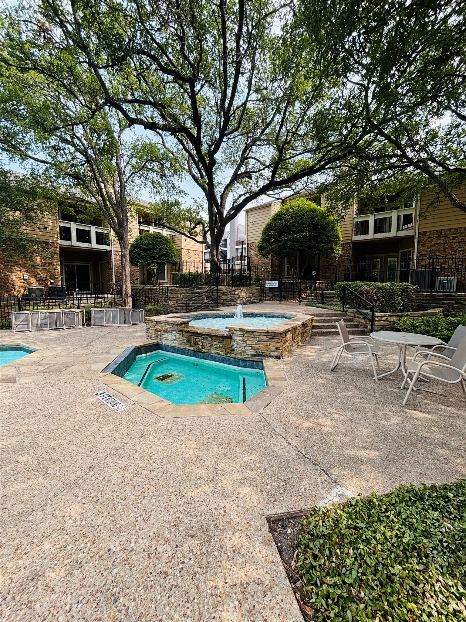 Courtyard area featuring a stone-clad fountain, two tiled spa pools, and exposed aggregate concrete surfacing