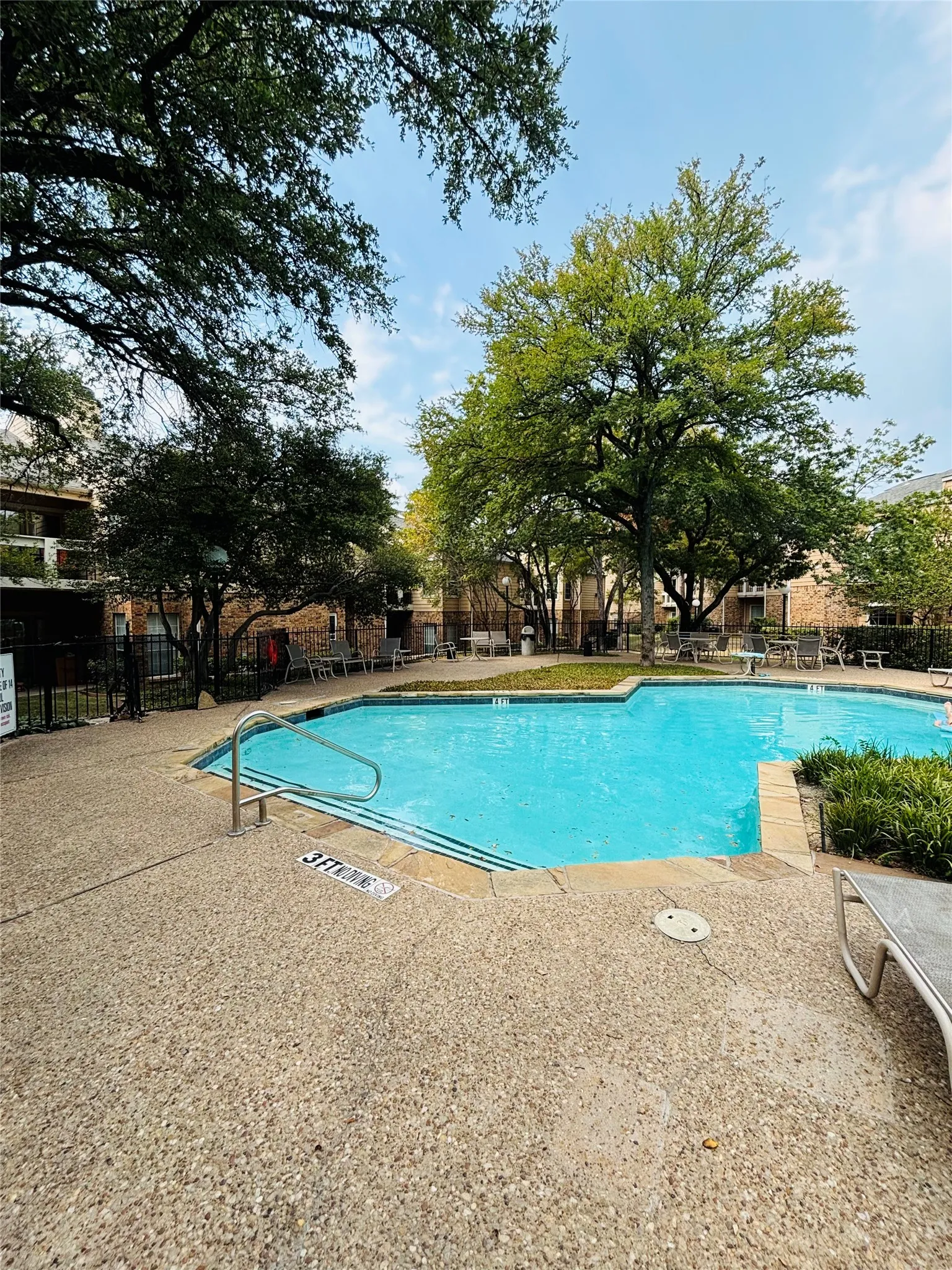 Sparkling in-ground swimming pool with integrated steps, surrounded by exposed aggregate concrete decking and mature trees