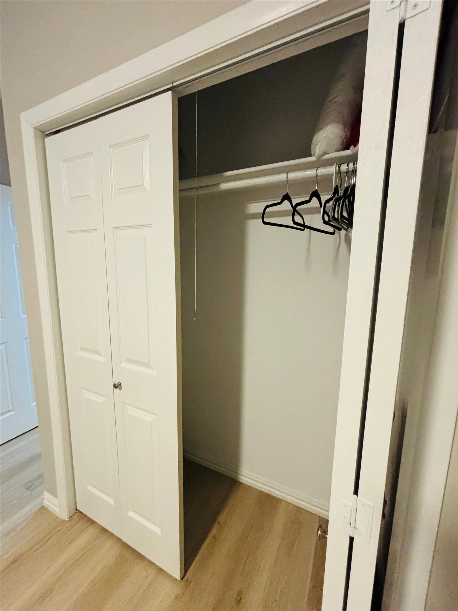 Built-in closet with bi-fold doors, hanging rod, and light wood-finish flooring