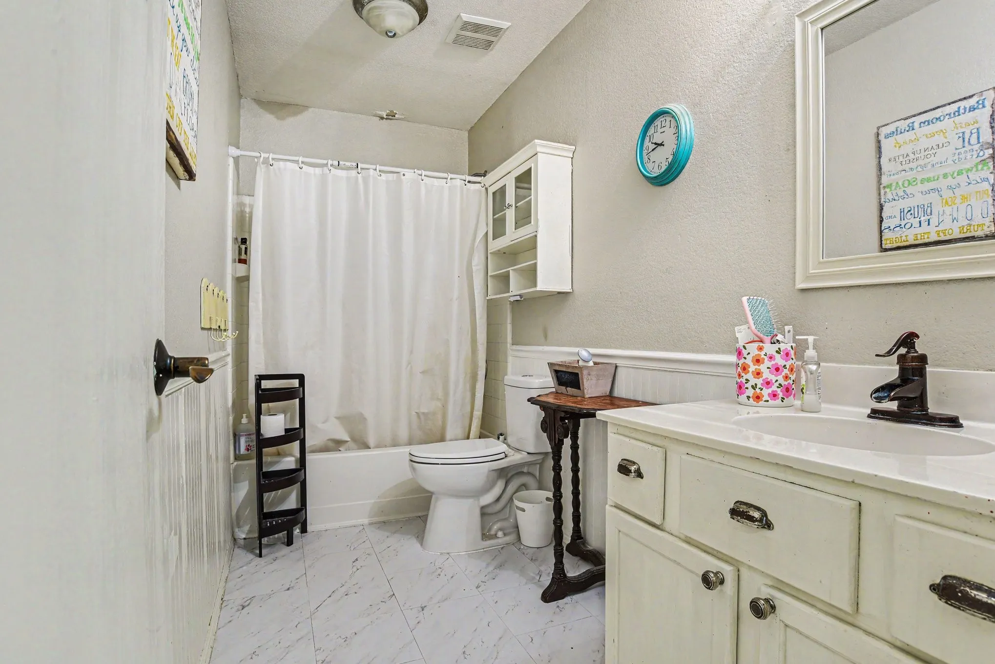 White tile flooring, white vanity with integrated sink, white bathtub, wall-mounted mirror, and beadboard wainscoting