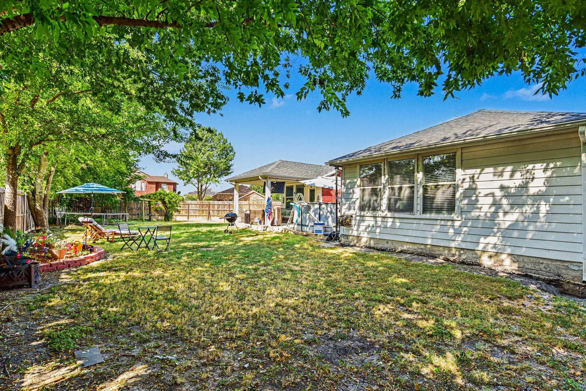 Expansive backyard featuring mature trees, a wooden privacy fence, and a covered patio area
