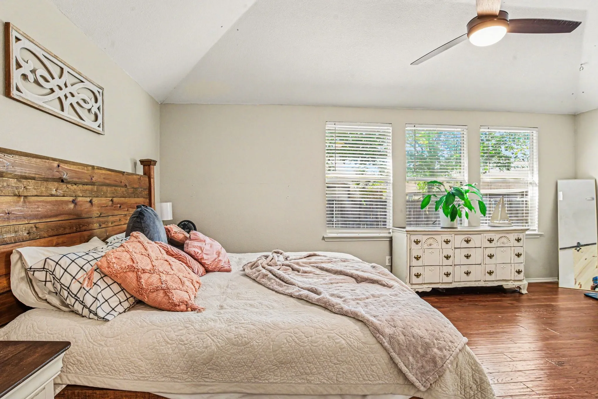 Vaulted ceiling with a ceiling fan, three windows with blinds, and wood-finish flooring