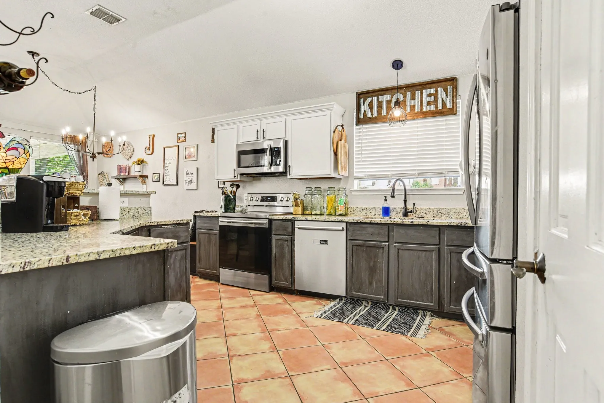 Kitchen featuring granite countertops, stainless steel appliances, two-tone cabinetry, a built-in chandelier, and terracotta-style flooring