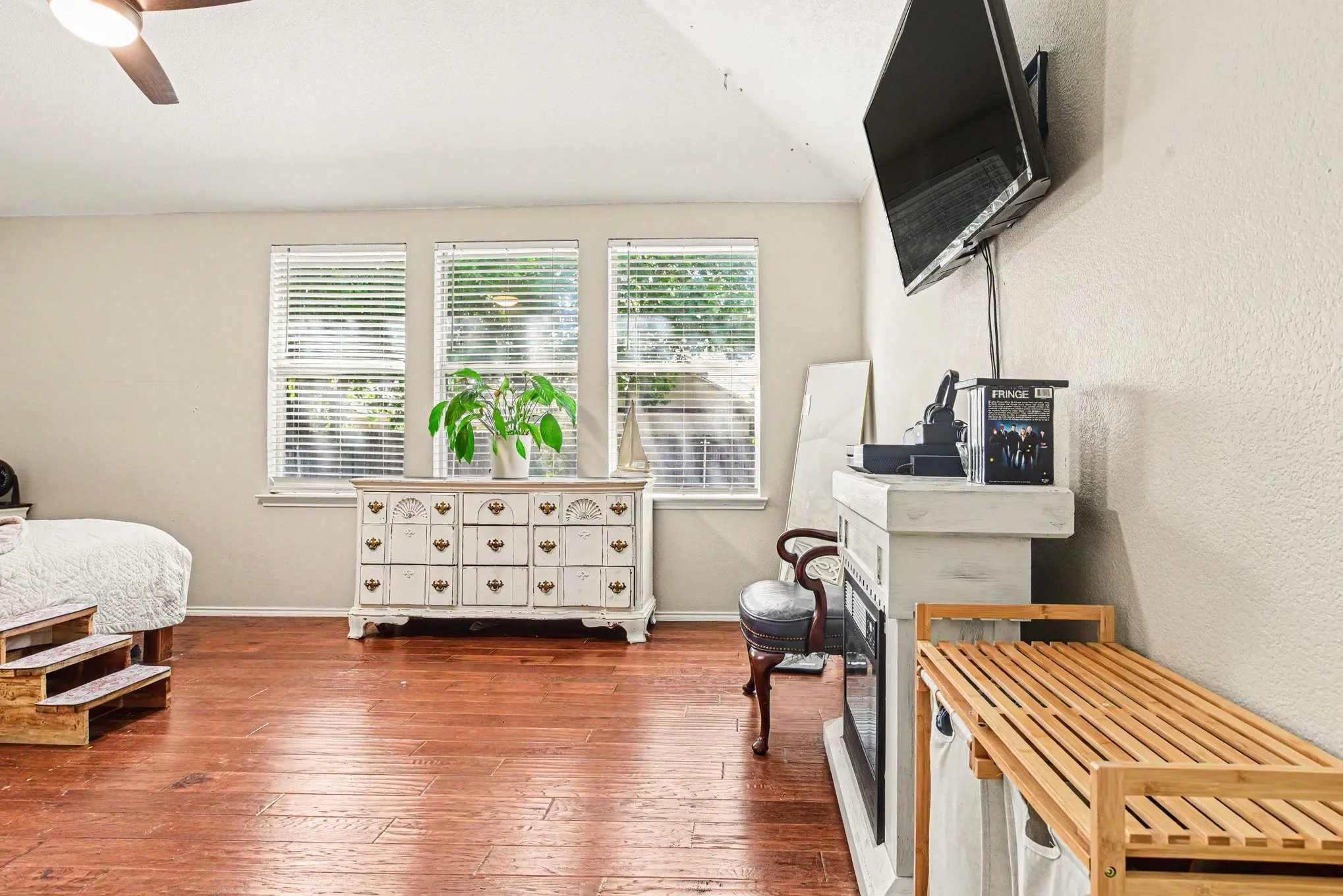 Vaulted ceiling with a ceiling fan, three windows with blinds, wood-finish flooring, and a built-in fireplace